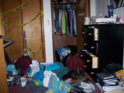 La imagen muestra una habitación muy desordenada, con ropa y libros en el suelo y cajones y armarios abiertos.