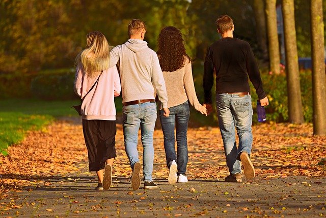 Cuatro amigos paseando en el parque, están de espaldas cogidos de la mano, el suelo está lleno de hojas de los árboles.