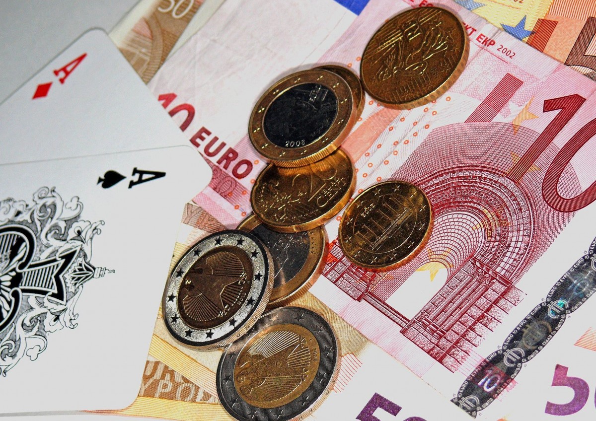 La imagen muestra monedas y billetes de euro junto con dos naipes.