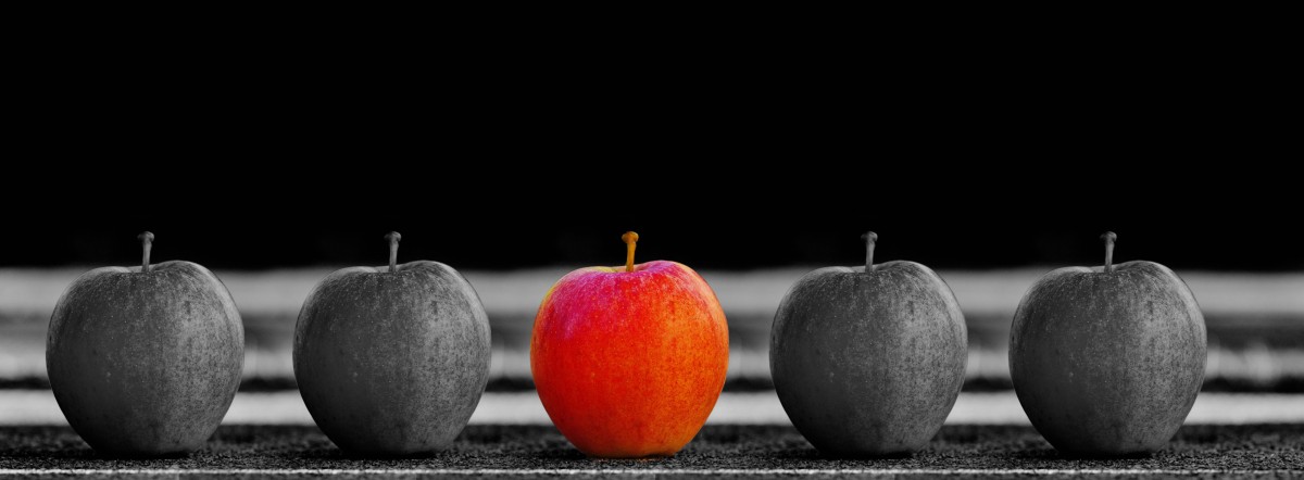 La imagen muestra cinco manzanas, dos a la izquierda negras, una en el centro roja y dos a la derecha negras.
