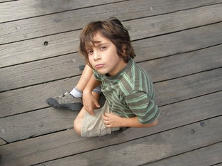La imagen muestra un niño sentado en el suelo mirando hacia la cámara que lo enfoca desde arriba.