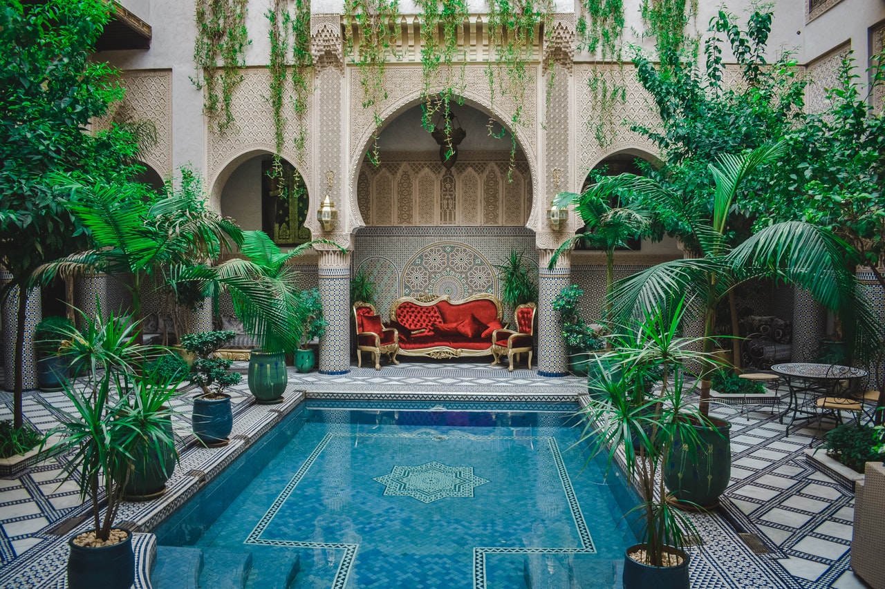 Patio árabe con una piscina en el centro y uno sofá y sillones en el fondo.