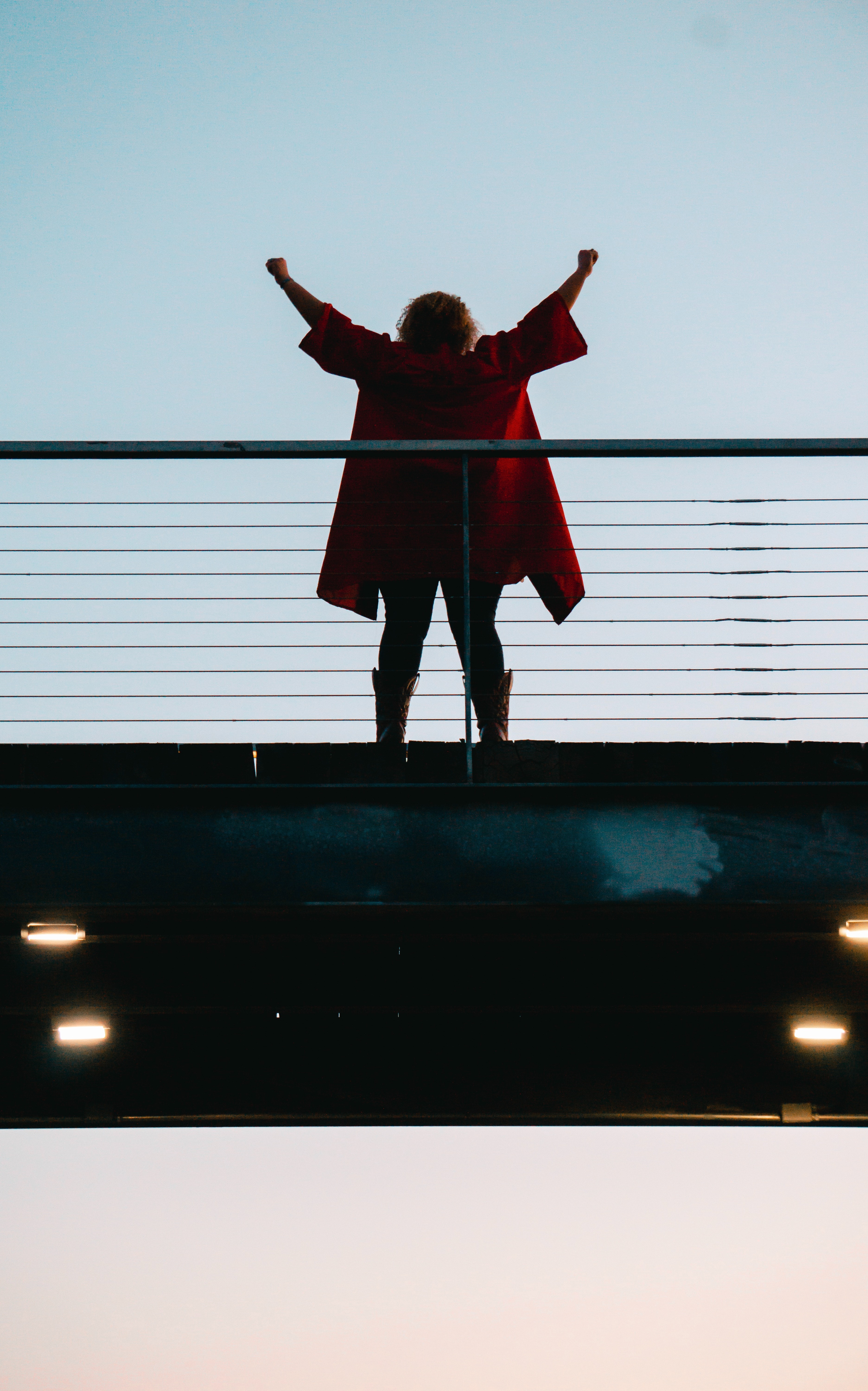 Chica en un puente alzando los brazos con abrigo rojo.