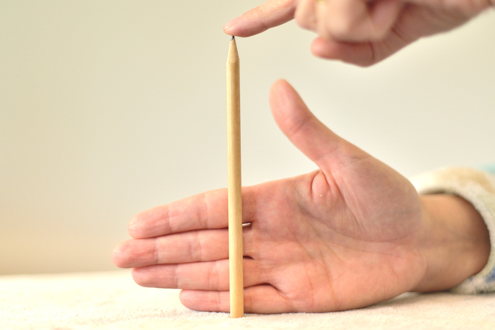 La imagen muestra un lápiz y una mano detrás, con cuatro dedos juntos, que está midiendo el lápiz