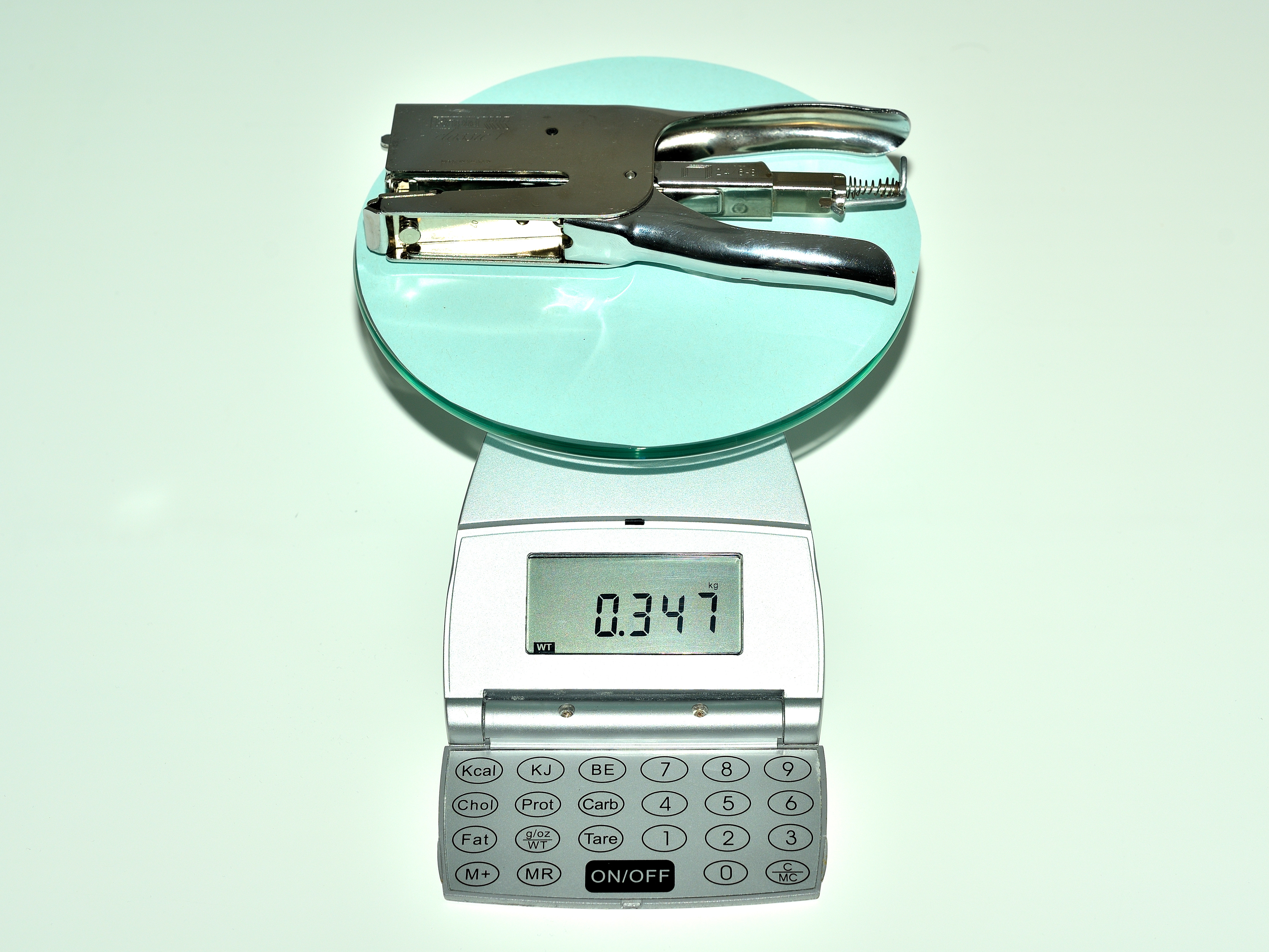 La imagen muestra una báscula, sobre la cual hay una grapadora metálica, que pesa 347 gramos