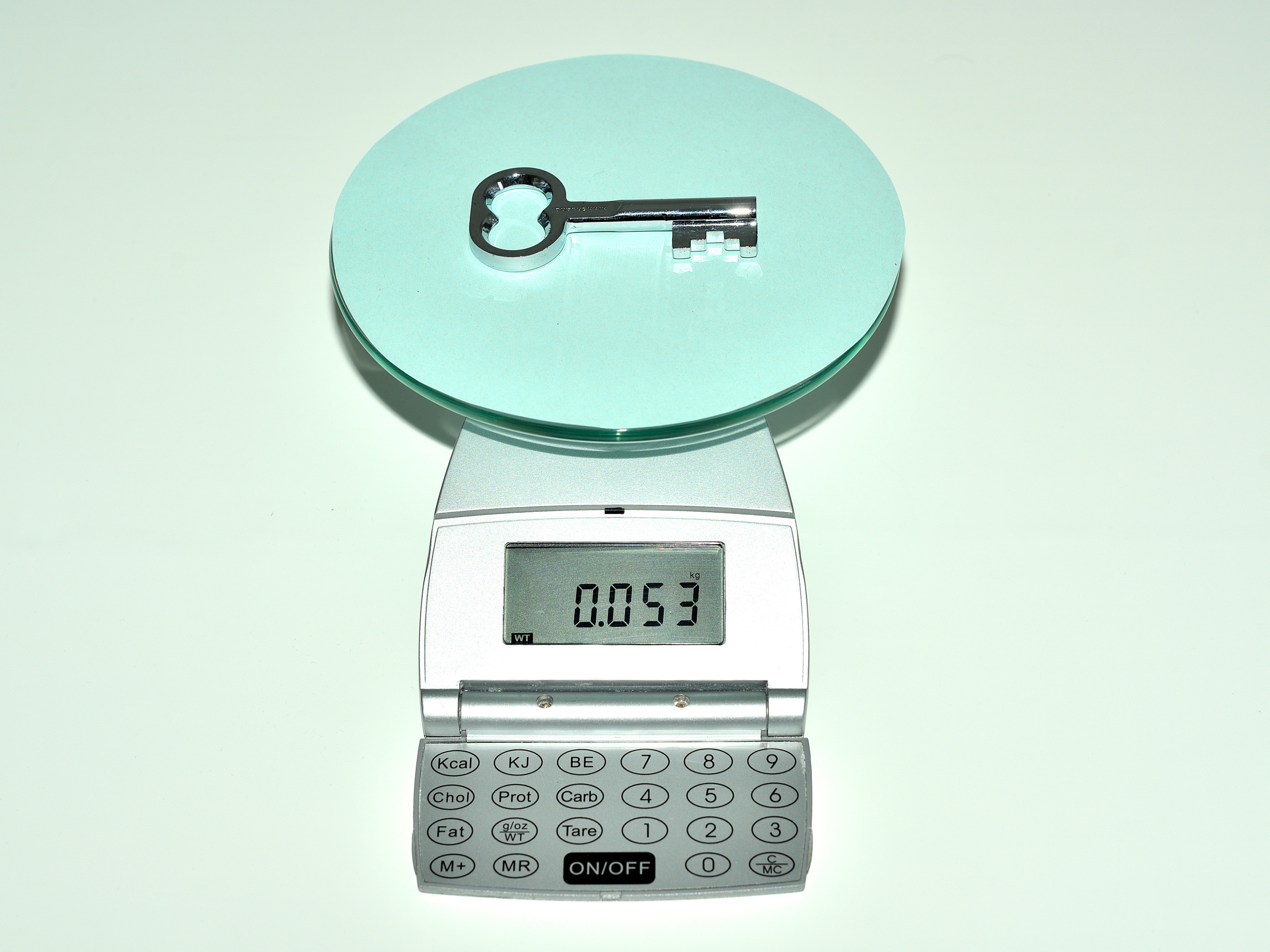 La imagen muestra una báscula, sobre la cual hay una llave metálica, que pesa 53 gramos