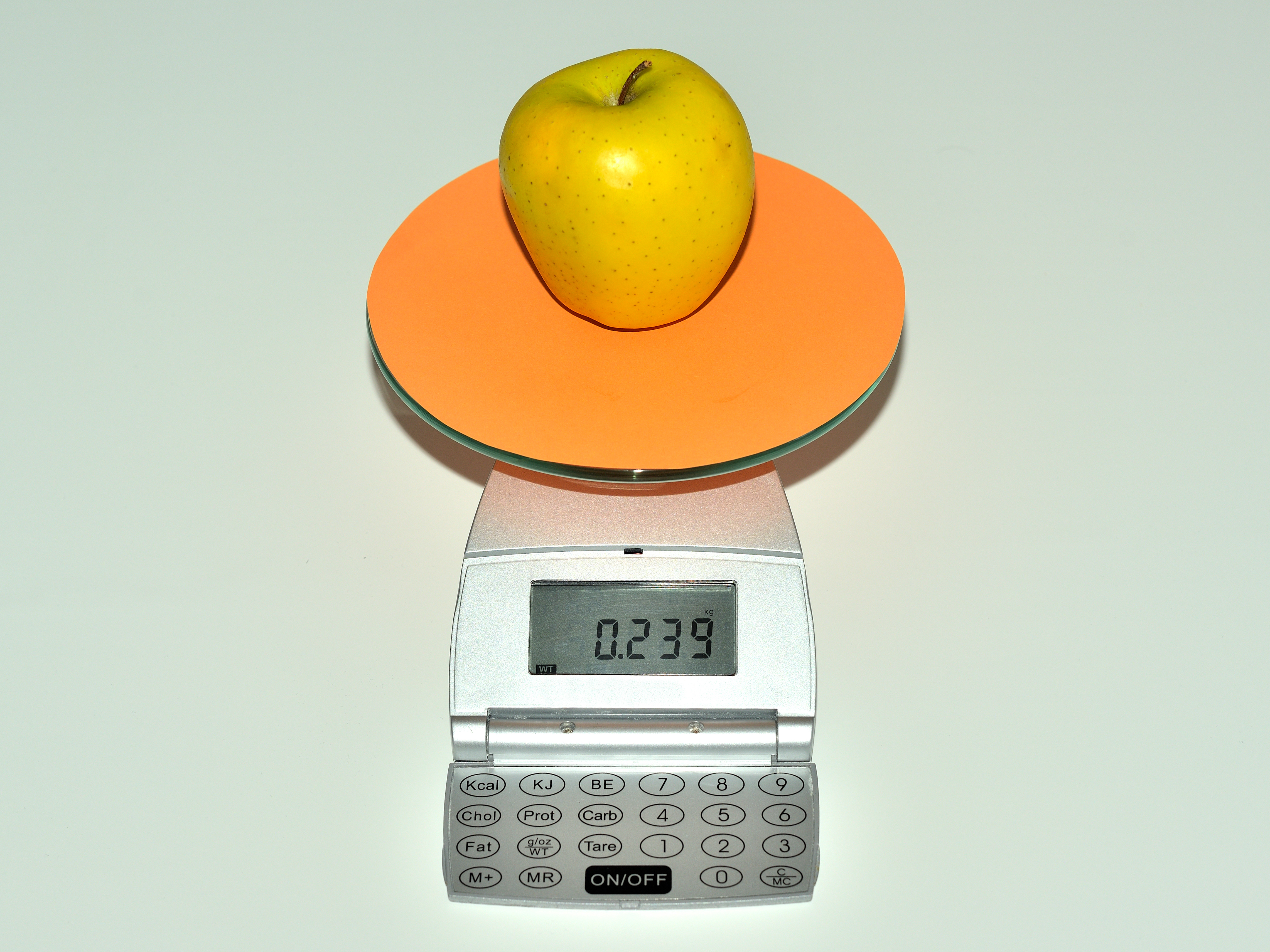 La imagen muestra una báscula, sobre la cual hay una manzana amarilla que pesa 239 gramos