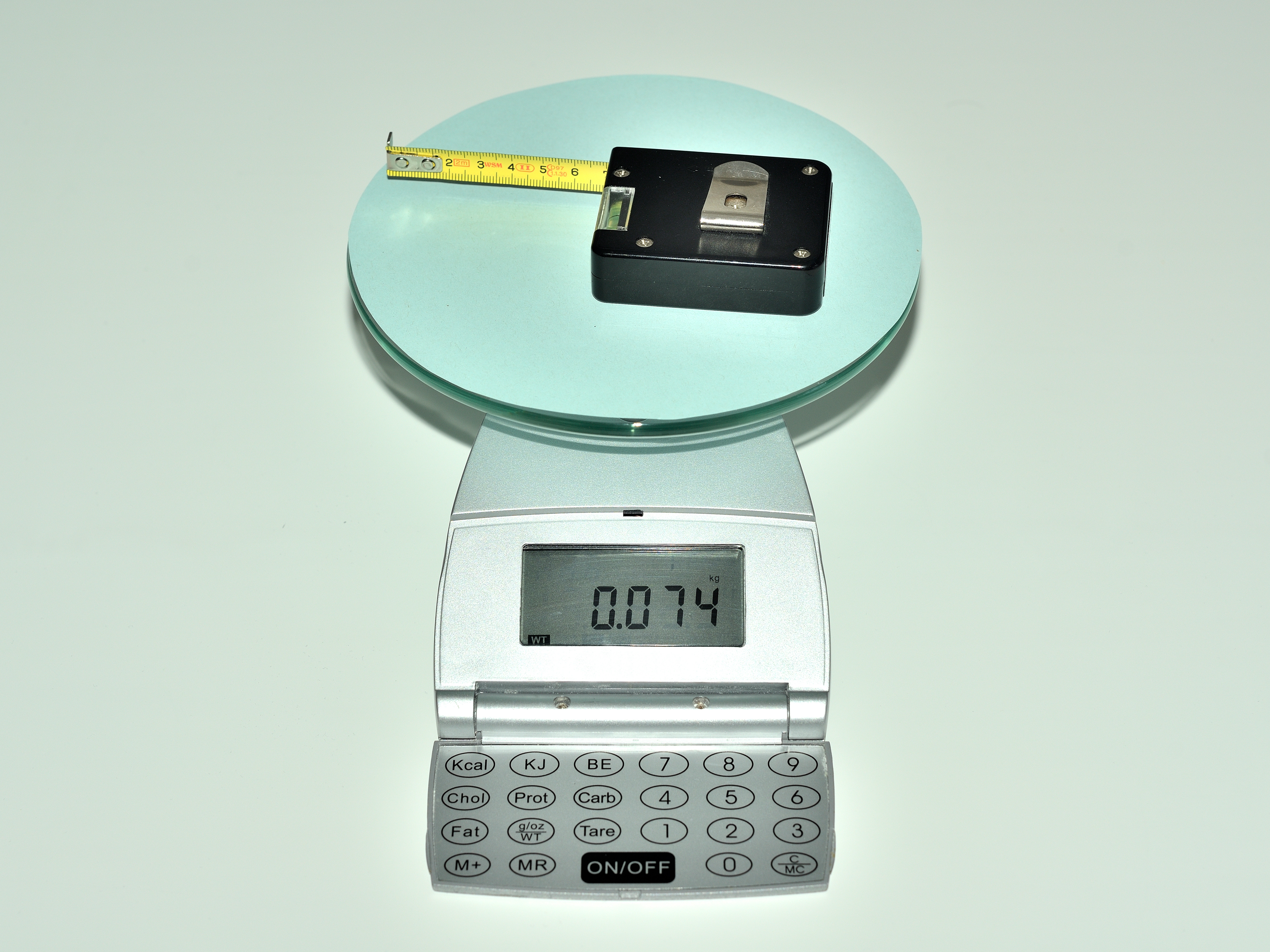 La imagen muestra una báscula, sobre la cual hay una cinta métrica que pesa 74 gramos