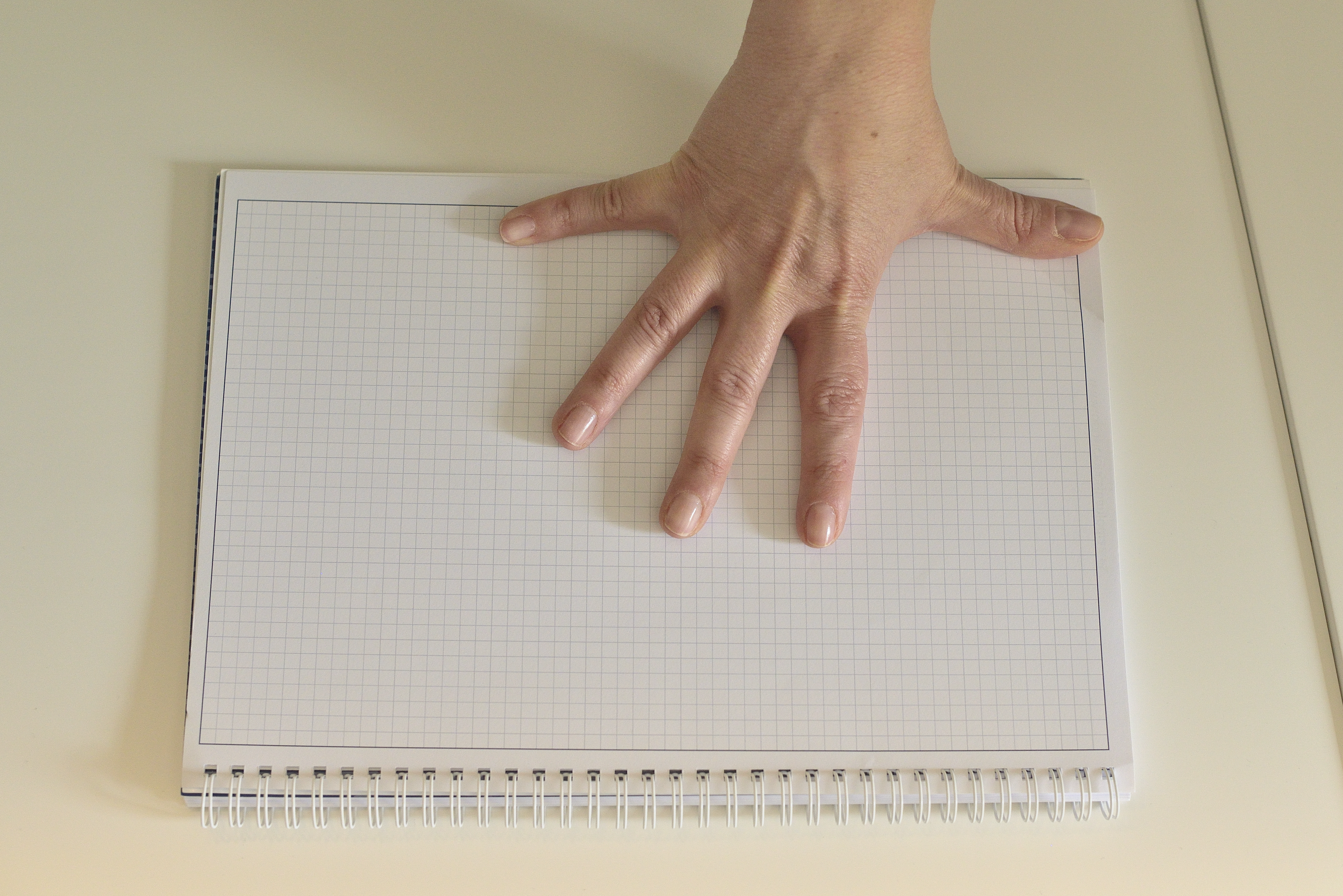 La imagen muestra una mano abierta en forma de palmo, que está midiendo un cuaderno que hay debajo