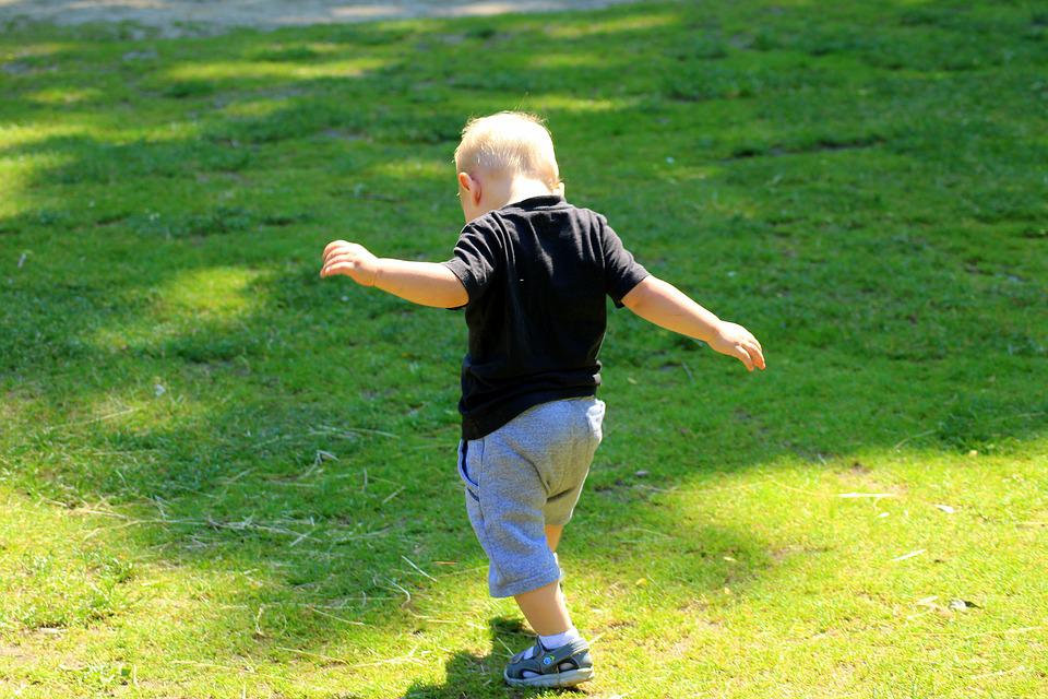 La imagen muestra un niño pequeño, de espaldas, que está andando por un campo de hierba verde