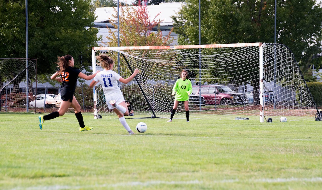 La imagen muestra a tres chicas jugando al fútbol en un campo de fútbol.