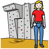 En la imagen se ve una mujer con arnés y detrás una pared para escalar con una cuerda.