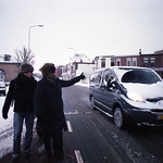 La imagen muestra un par de personas levantando un dedo al paso de un coche.