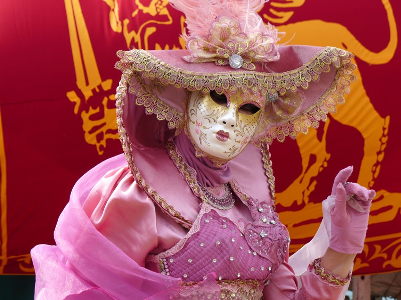 Una persona disfrazada de carnaval con un traje rosa y una máscara blanca. 