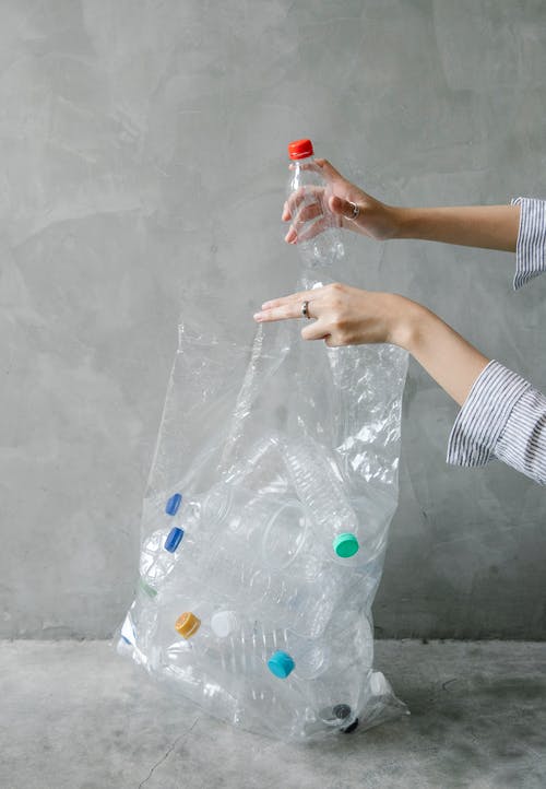 La imagen muestra una bolsa de plástico transparente llena de botellas de plástico y una mano que mete una botella más en la bolsa