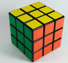 La imagen muestra un cubo de Rubik resuelto donde se observa una cara amarilla, otra naranja y otra de color verde. 