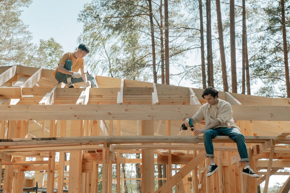 La imagen muestra a dos carpinteros haciendo la estructura de una casa. 