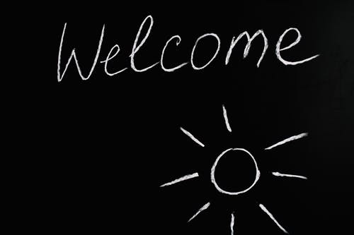 La imagen muestra una pizarra negra con la palabra Welcome y un sol pintado con tiza.