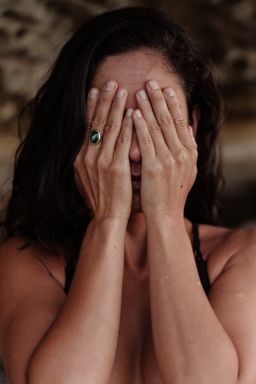 La imagen muestra una mujer que se tapa la cara con las dos manos.