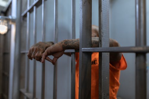 La imagen muestra un hombre vestido de naranja con los brazos sacados a través de los barrotes de una celda.