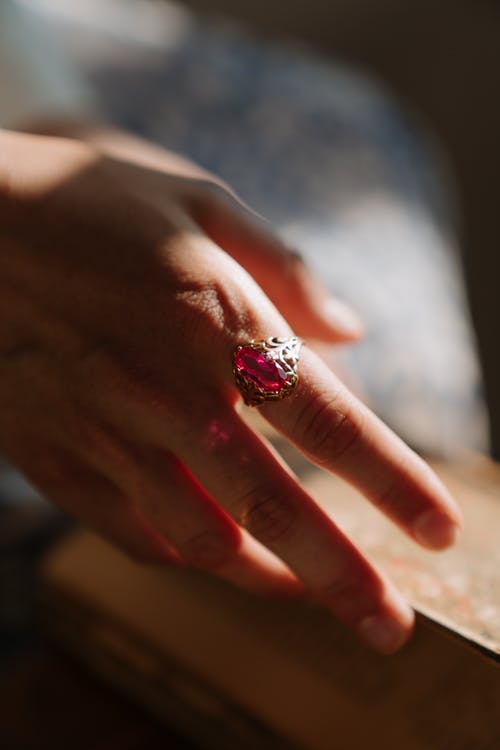 La imagen muestra una mano que lleva un anillo de oro con un rubí en el dedo índice.