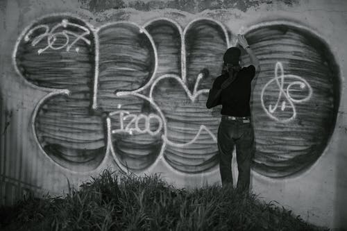 La imagen muestra a una chica de espaldas pintado un graffiti sobre un muro. 