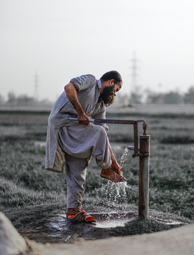 La imagen muestra un hombre sacando agua de un pozo con grifo para lavarse