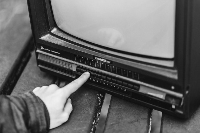 La imagen muestra una mano encendiendo una televisión en blanclo y negro. 