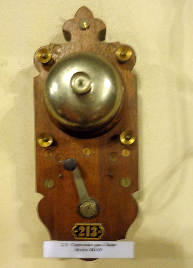 La imagen muestra un teléfono de madera con manivela, en la pared. 