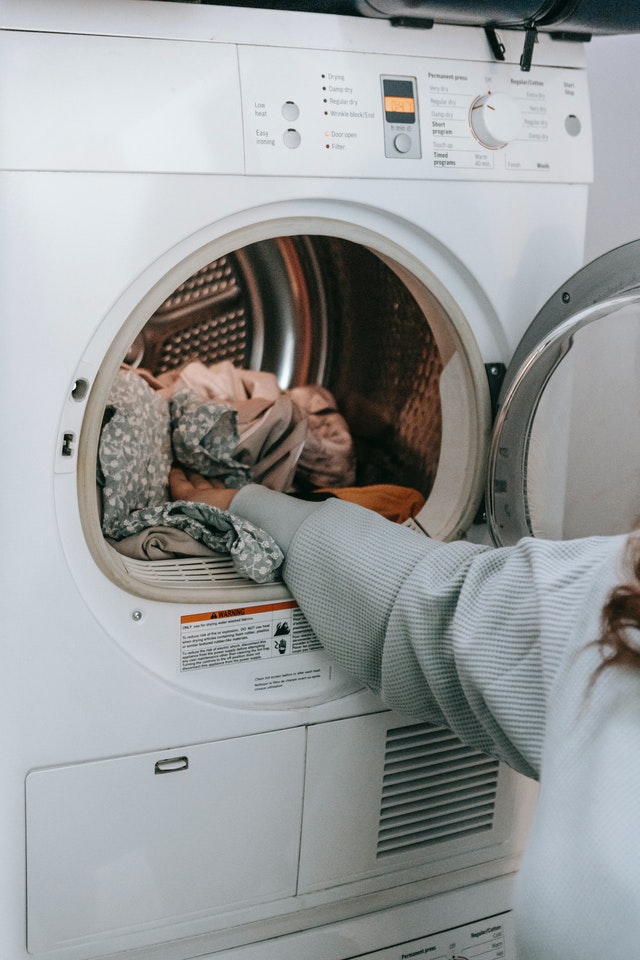 La imagen muestra una moderna lavadora y una mano cargándola de ropa para ser lavada.