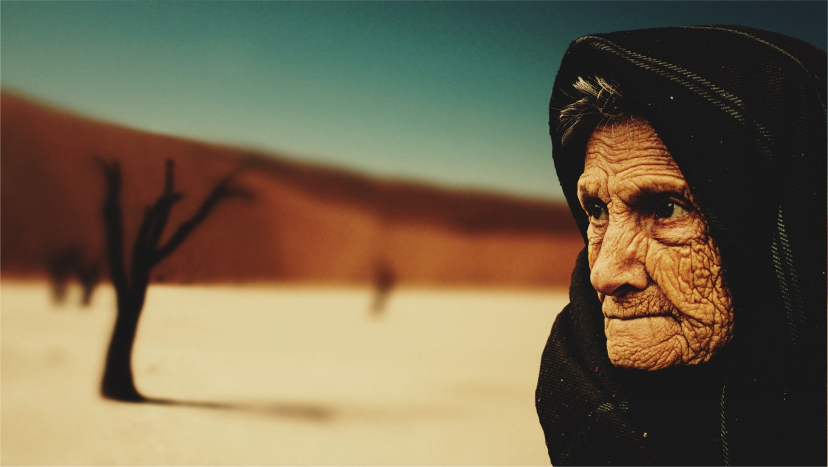 La imagen muestra a una anciana de perfil con un pañuelo sobre la cabeza y mirada perdida.