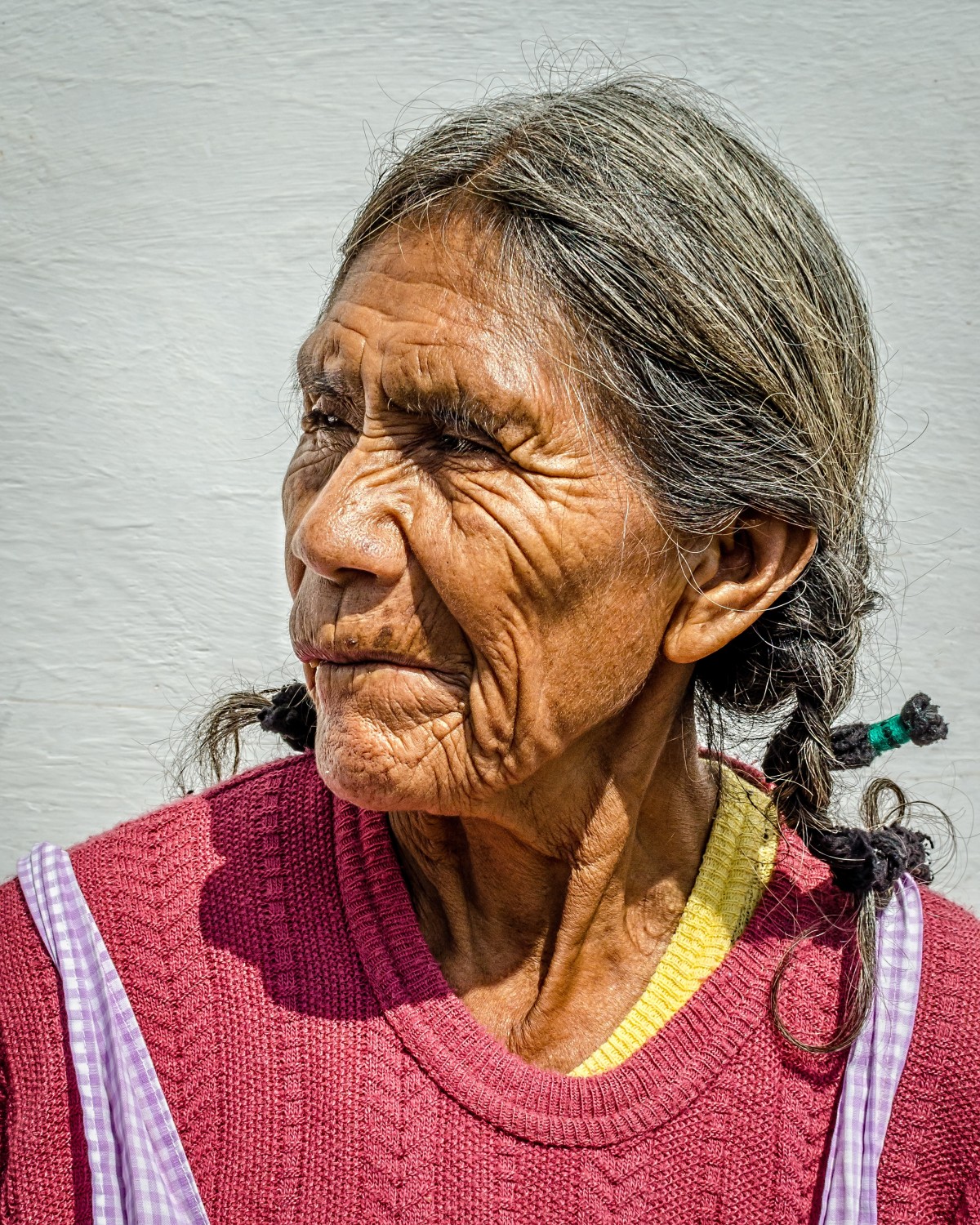 La imagen muestra la foto de una anciana a color con dos trenzas y mirando hacia un lado.