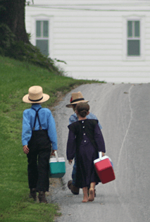 La imagen muestra tres niños andando de espaldas sosteniendo en su manos una nevera. 