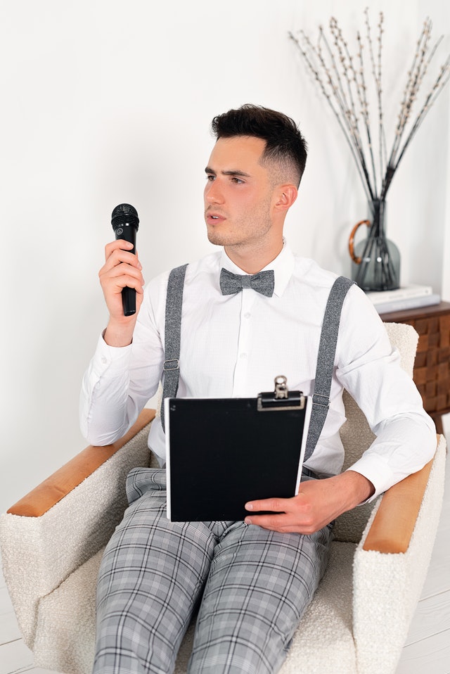 La imagen muestra un joven sentado con un micrófono en una mano y una carpeta en la otra en actitud pensativa.