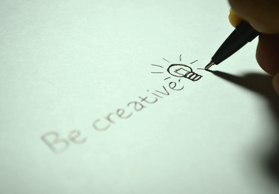 La imagen muestra la frase “ Be creative” en un papel con un dibujo de una bombilla