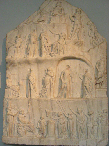 Estela que representa a poetas, musas y divinidades alabando a Homero que aparece en lo alto del relieve