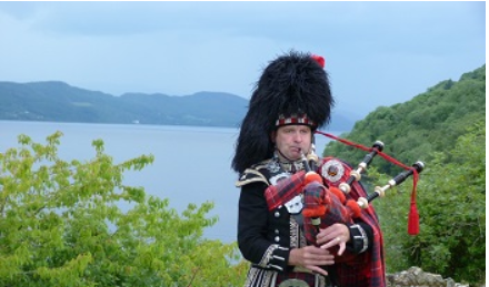 Imagen de un escocés, vestido con la falda típica escocesa tocando una gaita. Se ve el cuerpo entero de la cabeza a la cintura.