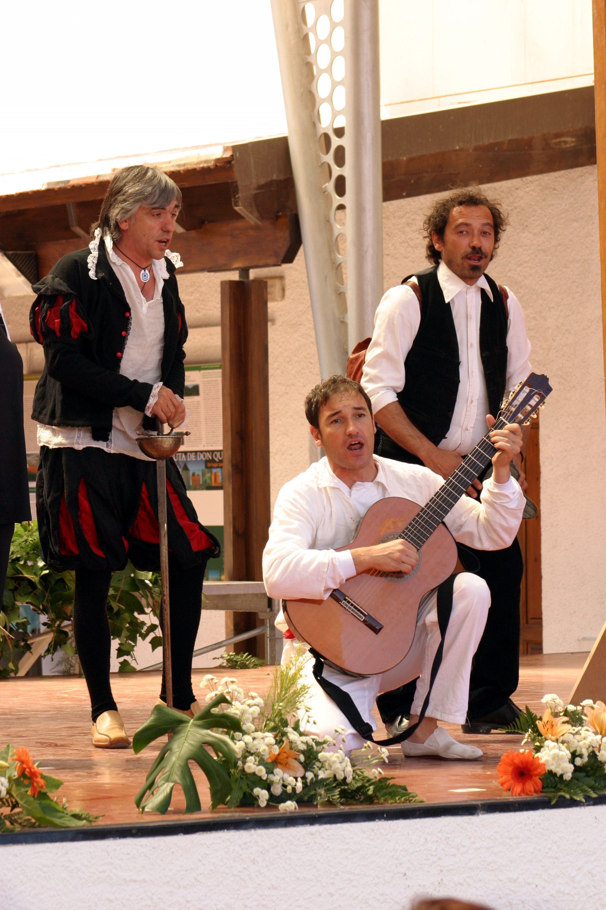 Escena donde aparecen tres hombres disfrazados, el del  medio aparece agachado tocando una guitarra.