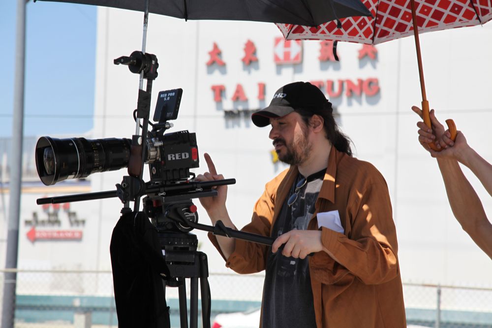 Esta imagen muestra a un hombre con barba y gorra que tiene delante una cámara para grabar películas.