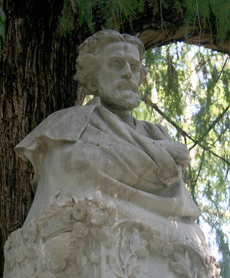 Estatua de mármol blanco de Gustavo Adolfo Bécquer bajo un árbol.