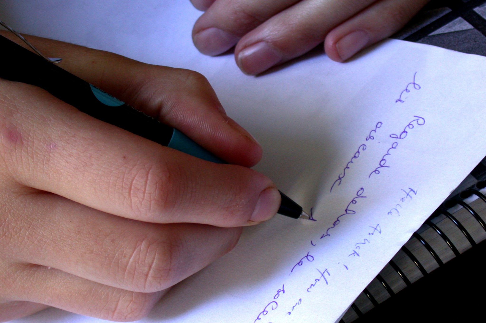 Esta imagen muestra una mano derecha que escribe mientras la izquierda se apoya en el papel