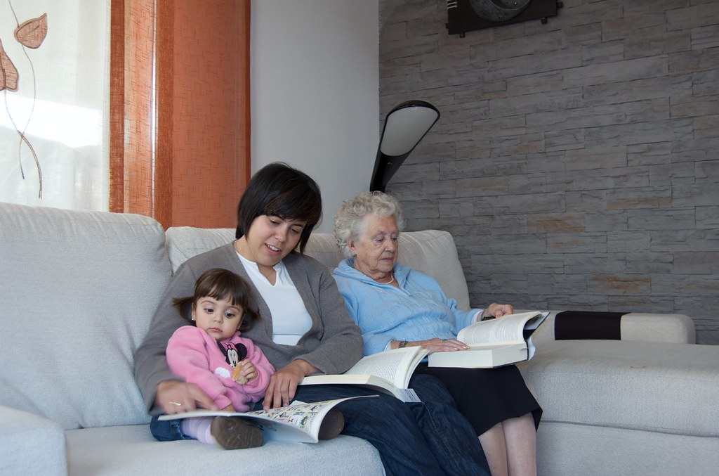 Esta imagen muestra a tres mujeres sentadas en un sofá, una es una niña, una mujer adulta y una anciana.