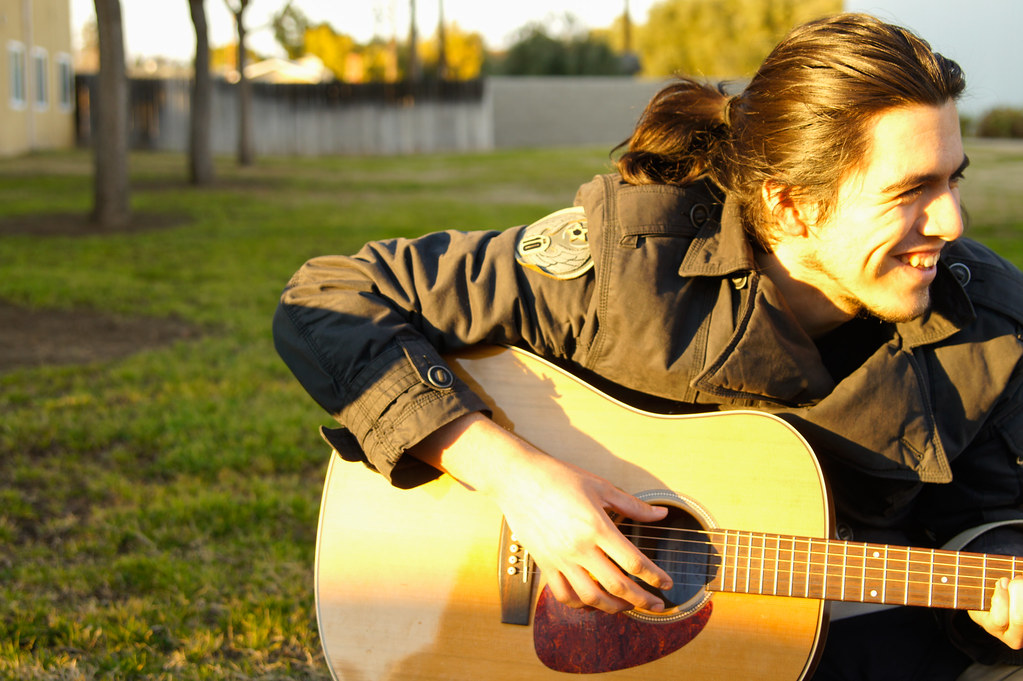 Esta imagen muestra a un chico sonriendo tocando la guitarra.