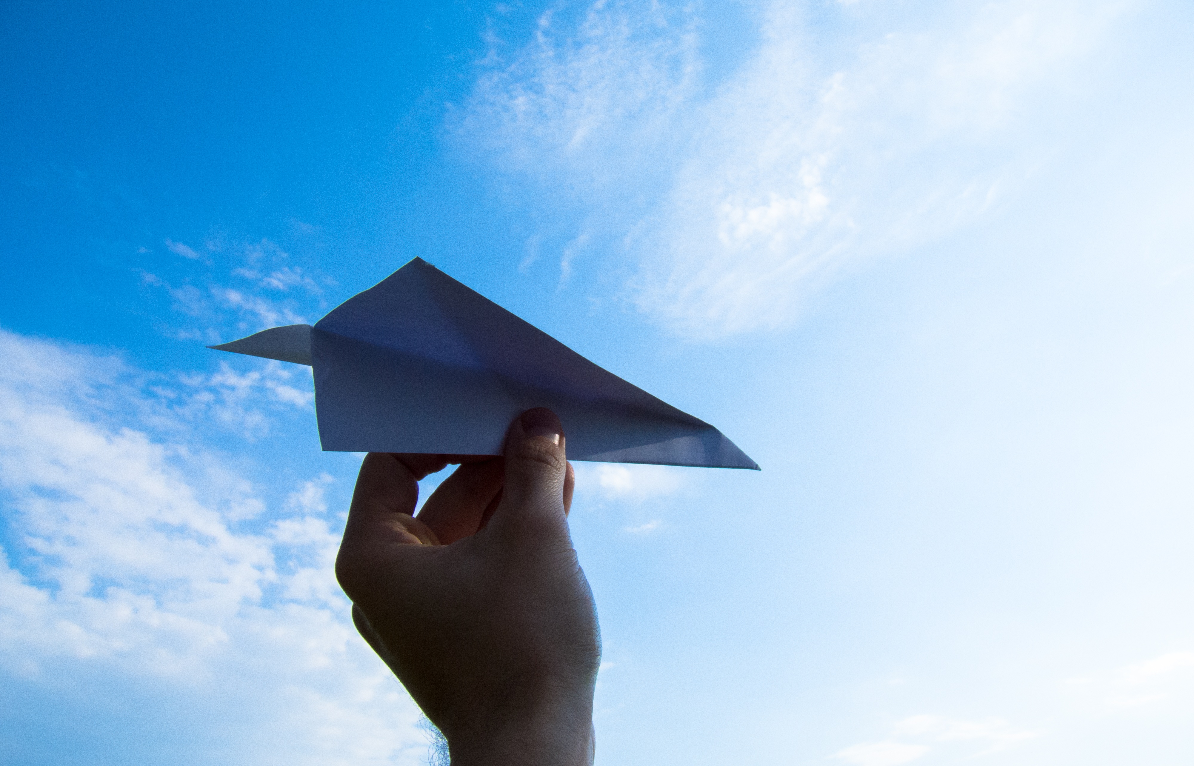 Mano que sujeta un avíon de papel, con el cielo azul de fondo